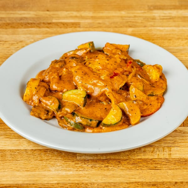 Italian dish with chicken and zucchini in a creamy orange sauce, served on a white plate.