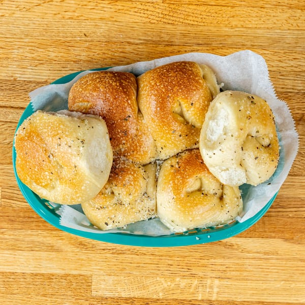 Basket of warm, golden-brown Italian bread knots, seasoned with herbs and salt, on a wooden table.