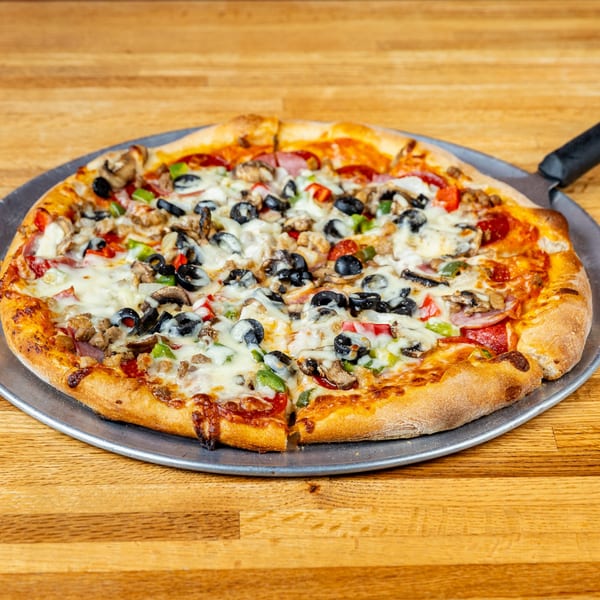 A freshly baked Tuscany Italian Restaurant pizza with various toppings on a metal pan.