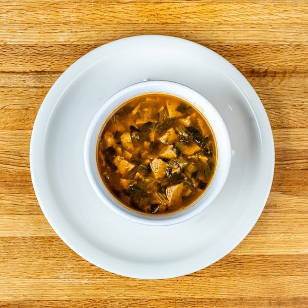 Overhead view of a white bowl filled with hearty Italian soup, featuring greens and meat, on a wooden table.