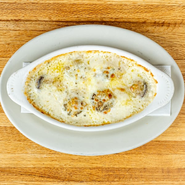 Baked clams oreganata, a classic Italian appetizer, served in a white oval dish on a wooden table.