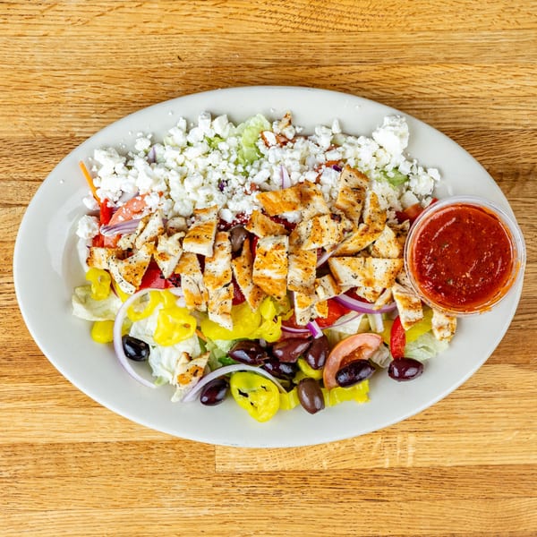 Grilled chicken salad with feta, olives, peppers, and red sauce on a white plate.